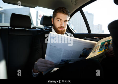 Serious bärtigen Geschäftsmann, sitzen im Auto mit Zeitung in Händen Stockfoto