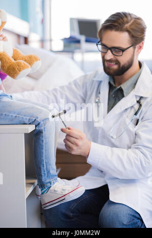 Lächelnde männlichen Arzt mit Reflexhammer auf Knie des kleinen Patienten Stockfoto