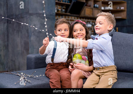 Zwei kleine Jungen und Mädchen sitzen auf dem Sofa halten Ostereier und Kätzchen Stockfoto