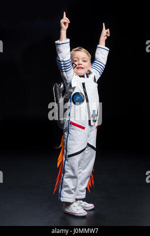 Kleiner Junge Astronauten im Raumanzug nach oben mit den Fingern auf schwarz Stockfoto