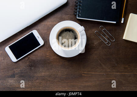 Draufsicht der Kaffeetasse, liefert Smartphone mit leerer Bildschirm, Notebook und Büro auf Holztisch Stockfoto