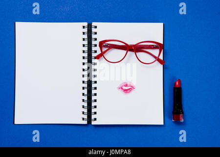 Draufsicht der stylische Brille auf Notebook und Lippenstift auf blau Stockfoto