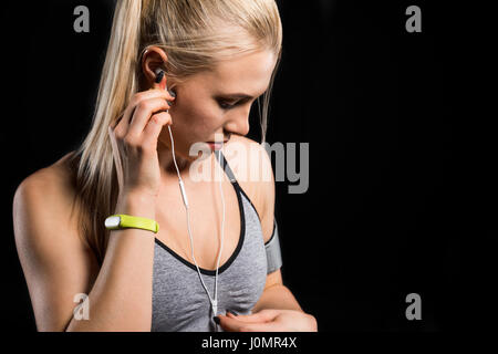 Porträt der sportlichen Frau mit Kopfhörern und Fitness-Tracker auf schwarz Stockfoto
