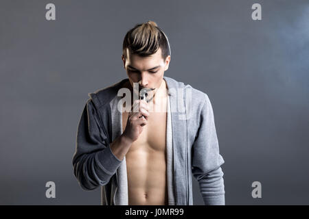 Schönen jungen Mann halten elektronische Zigarette und Dampfen auf grau Stockfoto