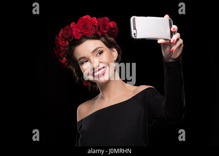 lächelnde Frau mit Rosen-Kranz am Kopf machen selfie Stockfoto