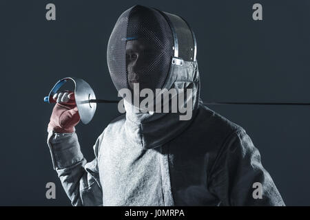 Porträt von professionellen Fechter im Fechten Maske mit Rapier auf grau Stockfoto