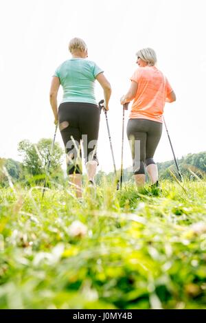 Zwei Frauen gehen in Gras mit Walking Stöcke, Ansicht von hinten. Stockfoto