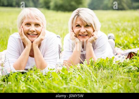 Zwei Frauen, die auf Gras mit den Händen auf das Kinn. Stockfoto