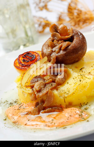 Gebratene Champignons mit Zwiebeln, Kartoffelpüree und Sauce auf Teller mit unscharfen Hintergrund Stockfoto