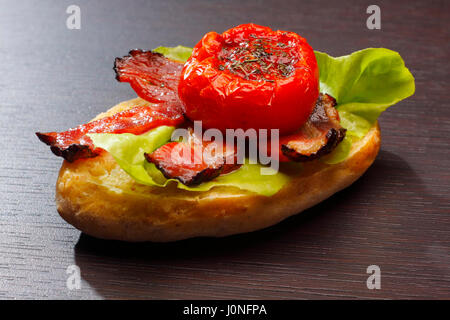 Ein halbes Brötchen mit gebratenem Speck, halbierte Tomaten und Salat Stockfoto