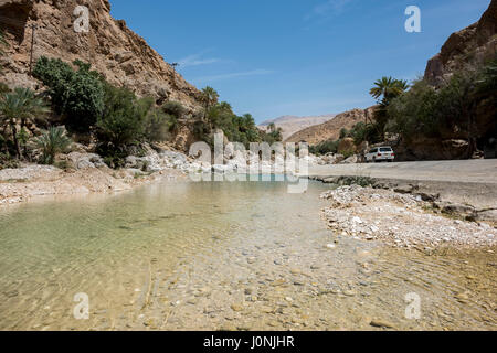 Ein Geländewagen, der eine abgelegene Straße neben einem Fluss in den trockenen Bergen des Oman fährt, perfekt für Abenteuer und Offroad-Reisen Stockfoto