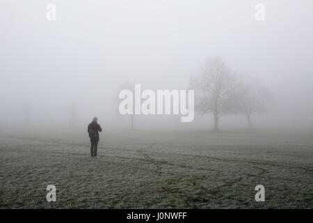 Junger Mann gekleidet in Winterkleidung Foto mit Handy Broomfield Park, London, verschwinden im Nebel an kalten Wintermorgen. Stockfoto