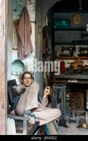 Krämer, Rauchen, ruht in einer Reparaturwerkstatt für altmodische Vintage Handkurbel Nähmaschinen, Pragpur Kulturerbedorf, Himachal Pradesh, Indien Stockfoto