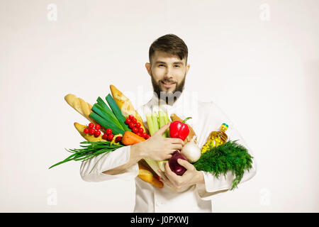 Lächeln auf den Lippen schön Koch mit Gemüse in Händen isoliert auf weißem Hintergrund. VEGANES ESSEN. Porträt von glücklich Profi-Koch mit Gemüse und Kräutern Stockfoto