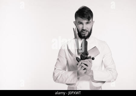 Studioaufnahme von einer glücklich bärtigen Jungkoch mit scharfen Messern über weißem Hintergrund. Koch mit Messer. Schön wütend schweren Einkauf halten viele scharf Stockfoto