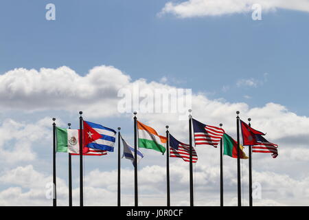 Die Flaggen USA, Nepal, Kamerun, Israel, Indien, Mexiko und Kuba auf einen Fahnenmasten im Wind gegen einen blauen Himmel und weiße Wolken. Der Wind weht. Stockfoto