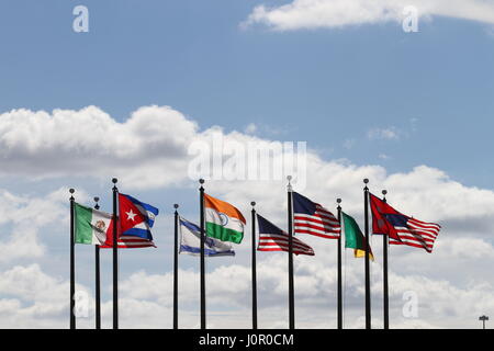 Die Flaggen USA, Nepal, Kamerun, Israel, Indien, Mexiko und Kuba auf einen Fahnenmasten im Wind gegen einen blauen Himmel und weiße Wolken. Der Wind weht. Stockfoto