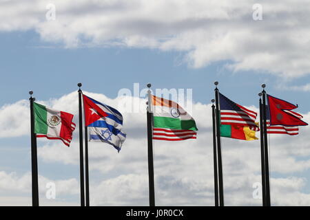 Die Flaggen USA, Nepal, Kamerun, Israel, Indien, Mexiko und Kuba auf einen Fahnenmasten im Wind gegen einen blauen Himmel und weiße Wolken. Der Wind weht. Stockfoto