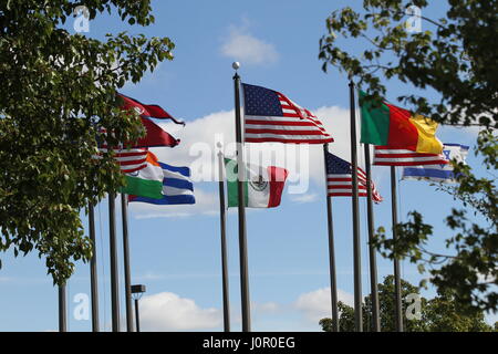 Die Flaggen USA, Nepal, Kamerun, Israel, Indien, Mexiko und Kuba auf einen Fahnenmasten im Wind gegen einen blauen Himmel und weiße Wolken. Der Wind weht. Stockfoto