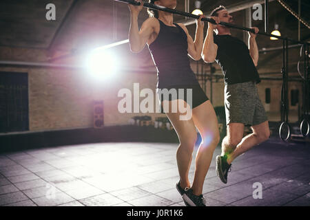Zwei junge sportliche Menschen tragen Sportswear Klimmzüge in helle geräumige Turnhalle zu tun. Stockfoto