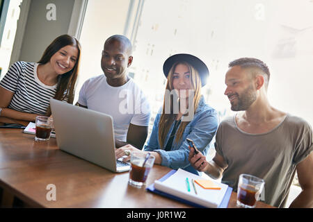 Junge hübsche Frauen mit drei Kollegen am Schreibtisch mit Laptop sitzen und Blick in die Kamera. Stockfoto