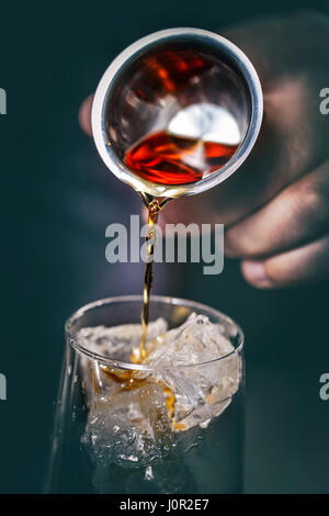 Barkeeper gießt Alkohol aus einem Messgerät Glas in ein Glas mit Eis Stockfoto