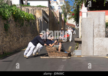 Touristen auf der Rodelbahn Monte, Madeira. Madeiras Rodeln werden auf der 2 km langen Fahrt von Monte nach Livra-Mento von Carreiros in Korbbooten gesteuert Stockfoto