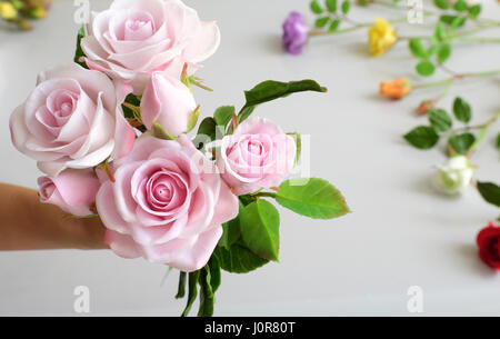 Wunderbare Ton Kunst, Frau Hand halten Strauß Rosen Blumen in Rosa auf weißem Hintergrund, schöne künstliche Blumen von Handwerkskunst mit geschickten Stockfoto