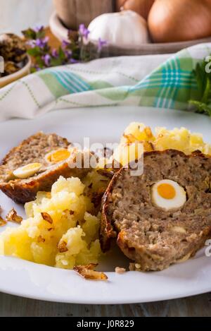 Vertikale Foto mit zwei Scheiben von hausgemachtem Ostern Hackbraten das ist von Wachteleiern gefüllt und serviert mit engmaschigen Netzen Zwiebeln Kartoffeln auf weißen Teller. INGRA Stockfoto