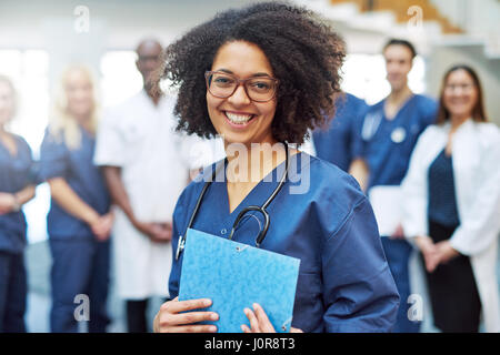 Lächelnde junge schwarze Ärztin stand vor der medizinischen Team im Krankenhaus Stockfoto