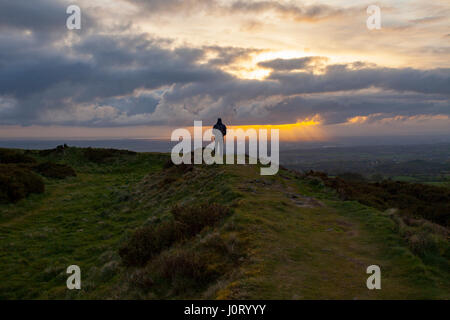 Dämmerungsaktiv Sonnenstrahlen brechen zwischen schweren Wolken über ländliche Flintshire in Wales in Richtung Cheshire in England in der Morgendämmerung als Person beobachtet das Spektakel auf Moel y bekräftige und Eisenzeit Wallburg Stockfoto