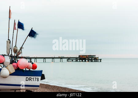 England, viel Strand. Heck des Fischerboot auf Kies, und im Boden zurück, Betonpfeiler. Das Meer ist ruhig, Dämmerung Himmel, schwache Band Pink von Horizon, grau vor. Stockfoto