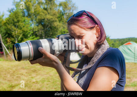 Eine junge Frau mit lila gefärbte Haare nimmt ein Foto mit einem Teleobjektiv. Stockfoto