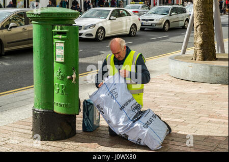 Die irische Post Postbote beim Entleeren eines Post Box und das Setzen der Buchstaben in einen Sack für Lieferung in Cork, Irland. Stockfoto