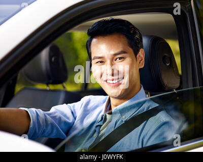 junge asiatische erwachsener Mann sitzen in einem Auto mit Sicherheitsgurt, Blick auf die Kamera zu Lächeln. Stockfoto