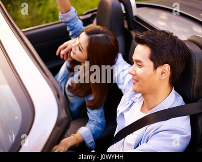 junge asiatische paar Fahrt in einem Cabrio Sport Auto bei Sonnenuntergang, hoher Winkel Ansicht. Stockfoto