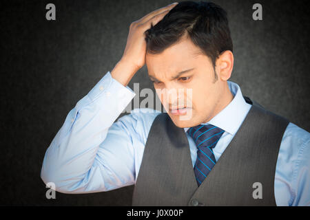 Closeup Portrait, gestresste junge Geschäftsmann mit Weste und Krawatte, die hand am Kopf mit Kopfschmerzen, isoliert grau schwarz. Negative menschliche Emotion Gesichts ex Stockfoto