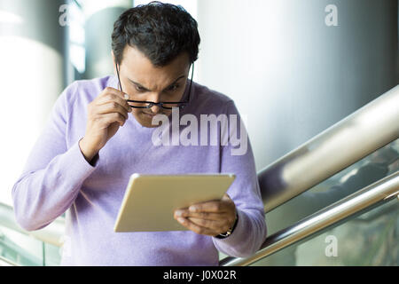 Closeup Portrait, sprachlos, verblüfft Mann in schwarzer Brille und lila Pullover, Augen, schielen, Anhebung der Augenbrauen, genauer Blick auf Tablet, Stockfoto