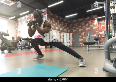 Seitenansicht des schönen jungen schwarzen Mann in Sportbekleidung und Kopfhörer tun stretching am gym Stockfoto