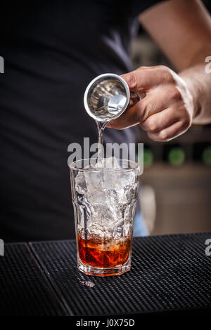 Barkeeper ist Alkohol aus einem Jigger in ein Glas über Eis gießen; Vorbereitung eine alkoholische cocktails Stockfoto