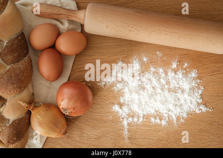 Brot mit Zwiebeln, Eiern, Mehl und einem Nudelholz auf einem Holztisch mit textfreiraum geflochten.  Food-Konzept Stockfoto