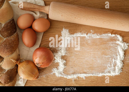 Brot mit Zwiebeln, Eiern, Mehl und einem Nudelholz auf einem Holztisch mit textfreiraum geflochten.  Food-Konzept Stockfoto