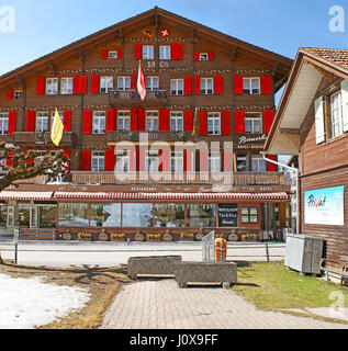 Das alte hölzerne Hotel und Restaurant, dekoriert mit hellroten Fensterläden und bemalten Mustern, befindet sich im Bergresort Wengen, Schweiz Stockfoto