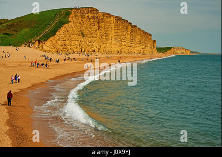 Menschen am Strand von West Bay an der Jurassic Coast in Dorset unter dem hoch aufragenden Felsen von Osten. Stockfoto