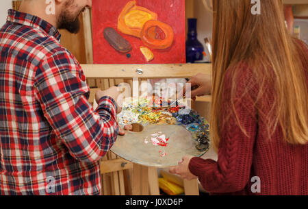 Künstler mit Spachtel und Holzpalette mit Ölfarben erklärt Student Regeln des Zeichnens Ölfarben. Stillleben in der Kunstschule zu schreiben. Kurs Stockfoto