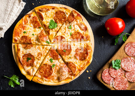 Peperoni-Pizza mit Zutaten - frische hausgemachte Pizza mit Salami, Käse und Tomatensauce und Zutaten auf rustikalen schwarzen Stein Hintergrund mit Stockfoto