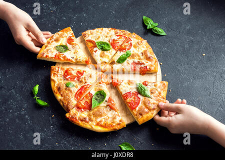 Menschen Hände nehmen Scheiben der Pizza Margherita. Pizza Margarita und Hände hautnah auf schwarzem Hintergrund. Stockfoto
