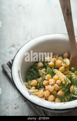 Salat mit Fusilli, Kichererbsen und Erbsen in Schüssel auf einem weißen Tisch vertikal Stockfoto