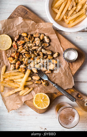 Muscheln mit Zitronen und Pommes auf dem vertikalen weißen Holztisch Stockfoto