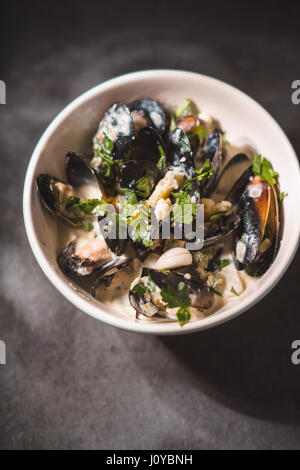 Muscheln in Schärpen in Sauce in einer Schüssel auf schwarzem Schiefer Stockfoto